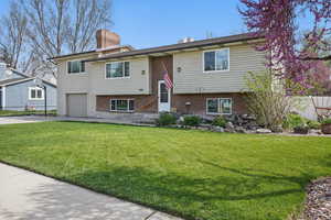 Bi-level home featuring concrete driveway, a chimney, a front lawn, an attached garage, and brick siding