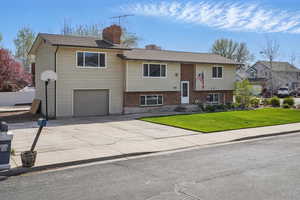 Bi-level home featuring a chimney, driveway, an attached garage, a front yard, and fence