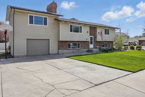 Split foyer home featuring a front yard, a garage, a chimney, concrete driveway, and brick siding