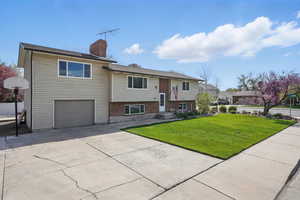 Split foyer home with an attached garage, a chimney, brick siding, a front lawn, and driveway