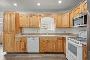 Kitchen with plenty of natural light, white appliances, light countertops, a sink, and wood finished floors
