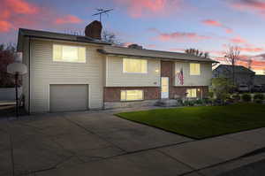 Bi-level home with a lawn, a garage, a chimney, brick siding, and driveway