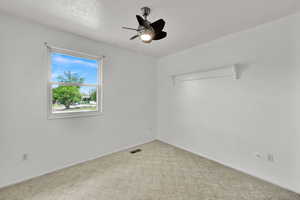 Carpeted empty room featuring ceiling fan, baseboards, and attic access