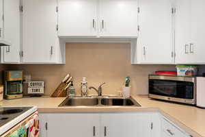 Kitchen featuring stainless steel microwave, light countertops, a sink, and white cabinetry