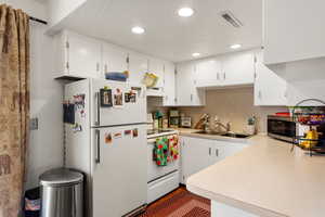 Kitchen with recessed lighting, white appliances, light countertops, under cabinet range hood, and a sink
