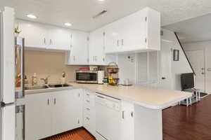Kitchen featuring stainless steel microwave, a peninsula, light countertops, white dishwasher, and a sink