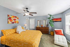 Carpeted bedroom with a textured ceiling, baseboards, and ceiling fan