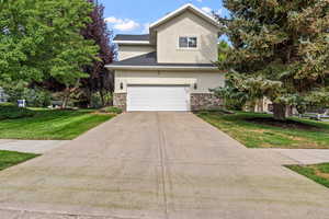 Traditional home featuring stucco siding, stone siding, concrete driveway, and a front yard
