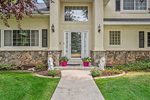 Doorway to property with stone siding, stucco siding, roof with shingles, and a yard