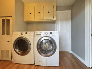 Washroom with washing machine and dryer, baseboards, wood finished floors, and cabinet space
