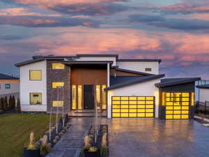 Modern home with an attached garage, stone siding, driveway, and stucco siding