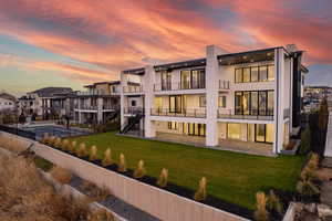 Back of house at dusk featuring stairs, a fenced backyard, stucco siding, a balcony, and a patio area