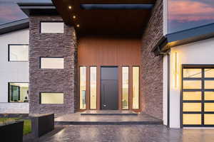 Exterior entry at dusk with stone siding, a patio area, and a garage