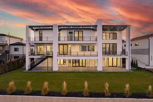 Back of house at dusk featuring a yard, stucco siding, a balcony, and stairs