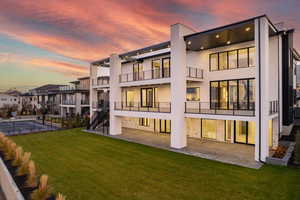 Back of property with stucco siding, a balcony, stone siding, and a patio