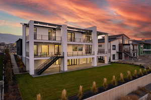 Back of house at dusk with stairway, stucco siding, a lawn, and a balcony