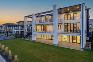 Rear view of property featuring a lawn, stucco siding, stairway, a balcony, and a patio