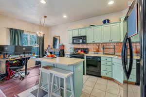 Kitchen with green cabinets, a center island, light countertops, backsplash, and black appliances