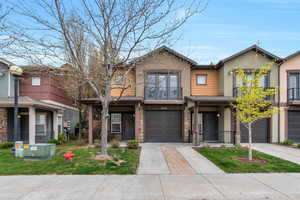 View of front of property with stone siding, a garage, concrete driveway, stucco siding, and a balcony