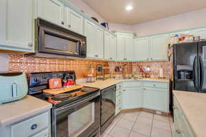 Kitchen with light countertops, backsplash, and black appliances