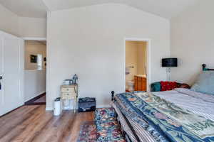 Bedroom featuring baseboards, light wood-style floors, ensuite bath, and lofted ceiling