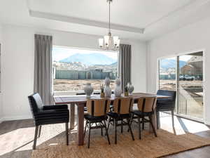 Dining room with a tray ceiling, a chandelier, wood finished floors, a mountain view, and baseboards