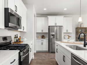 Kitchen with white cabinets, a sink, appliances with stainless steel finishes, dark wood-style floors, and light stone counters