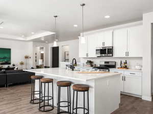 Kitchen with open floor plan, a kitchen island with sink, a kitchen bar, dark wood-style floors, and stainless steel appliances
