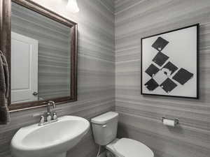 Bathroom featuring toilet, wallpapered walls, and a sink
