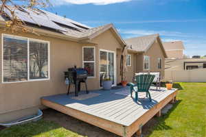 Rear view of property featuring a deck, stucco siding, fence, and a lawn