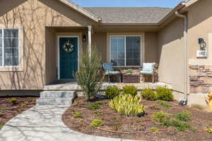 Doorway to property featuring stucco siding, stone siding, a shingled roof, and covered porch