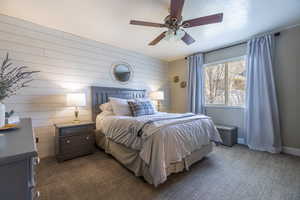 Bedroom featuring wood walls, baseboards, a ceiling fan, and dark colored carpet