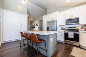 Kitchen with a center island, dark wood finished floors, stainless steel appliances, backsplash, and lofted ceiling