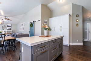 Kitchen with dark wood finished floors, ceiling fan, a barn door, and lofted ceiling