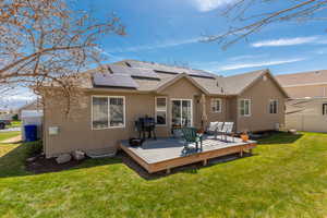 Rear view of property featuring roof mounted solar panels, a wooden deck, a yard, stucco siding, and fence