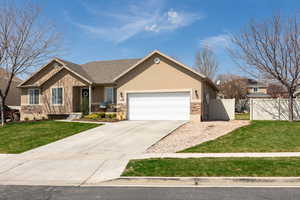 View of front of home with stucco siding, stone siding, a front lawn, a garage, and fence