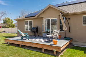 Back of house featuring a wooden deck, stucco siding, fence, and a lawn