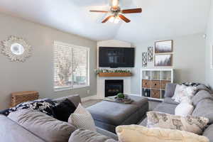 Carpeted living area featuring baseboards, a ceiling fan, a glass covered fireplace, and lofted ceiling