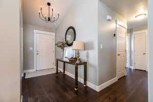Foyer entrance featuring baseboards, vaulted ceiling, an inviting chandelier, and hardwood / wood-style flooring