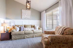 Living area featuring a decorative wall, carpet, wainscoting, and vaulted ceiling