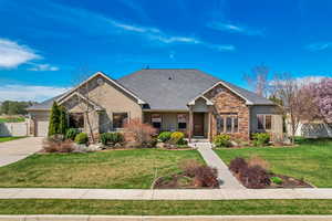 View of front facade with stucco siding, fence, stone siding, a front lawn, and an attached garage