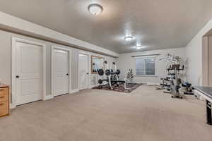 Workout room with baseboards, light colored carpet, and a textured ceiling