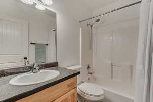 Bathroom featuring toilet, shower / bathtub combination with curtain, and vanity