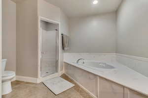 Bathroom featuring a garden tub, toilet, a stall shower, baseboards, and tile patterned floors