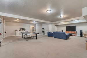 Recreation room with baseboards, carpet flooring, and a textured ceiling
