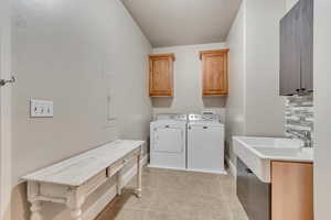 Laundry area with baseboards, a textured ceiling, cabinet space, washing machine and dryer, and light tile patterned flooring