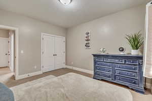Carpeted bedroom with a textured ceiling, a closet, and baseboards