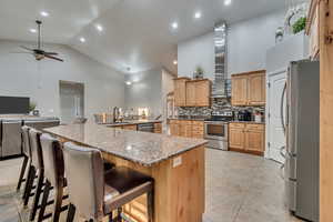 Kitchen with a sink, ceiling fan, appliances with stainless steel finishes, decorative backsplash, and high vaulted ceiling