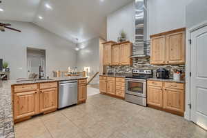 Kitchen with ceiling fan, high vaulted ceiling, wall chimney range hood, a sink, and stainless steel appliances