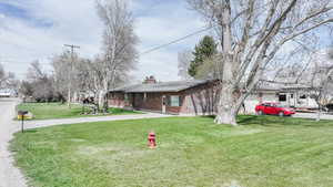 Ranch-style home with a front yard, brick siding, driveway, and a chimney